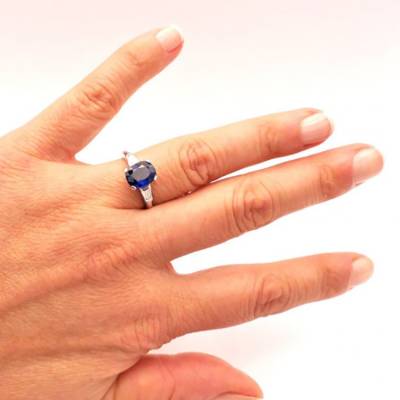 Anillo oro blanco con diamantes y zafiro de color azul en mano de modelo